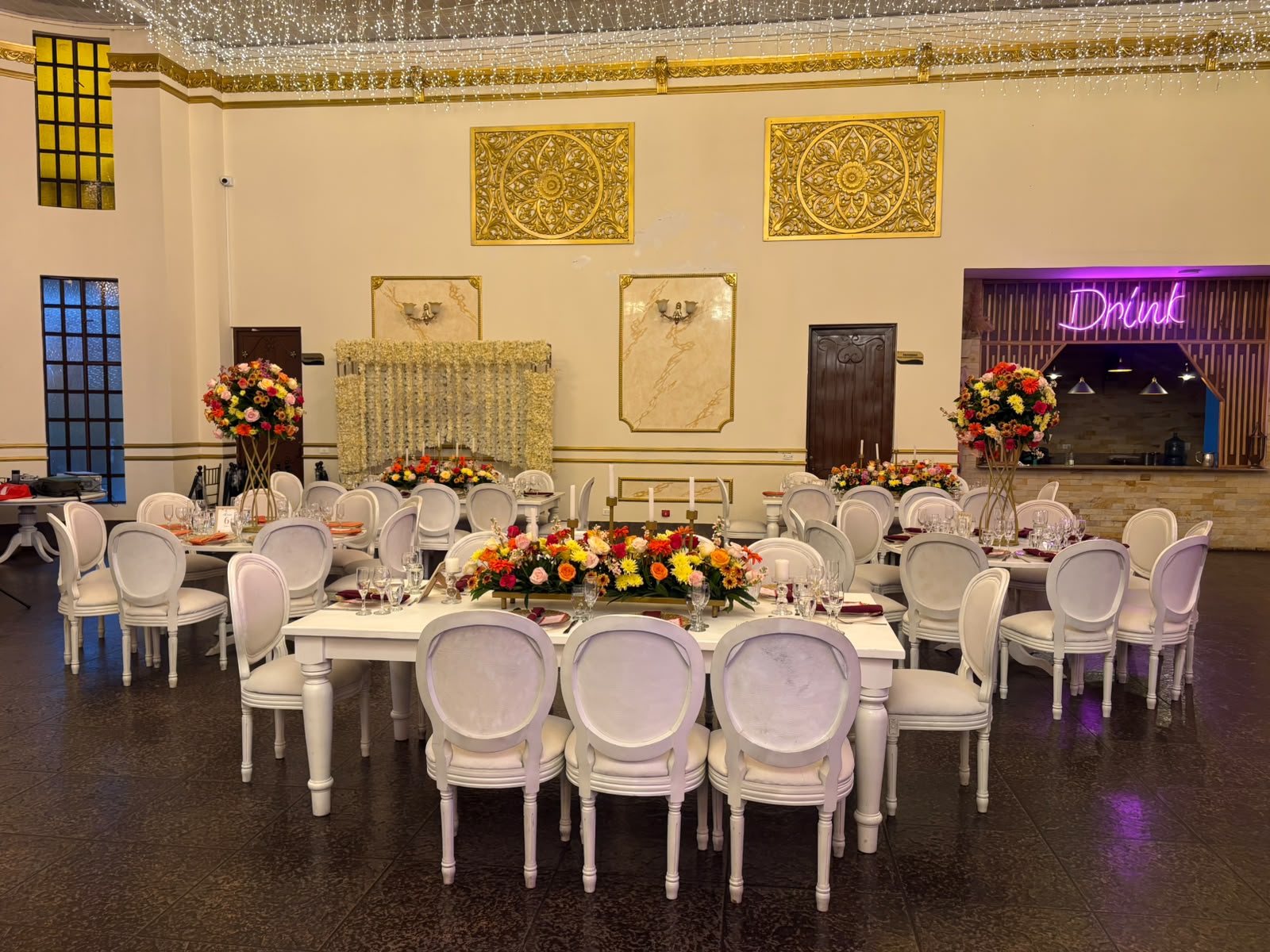 Salón con barra de bebidas iluminada y decoración floral